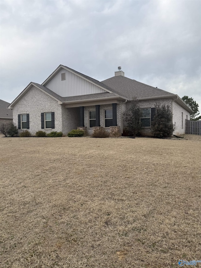 ranch-style home featuring a shingled roof, a front lawn, brick siding, and a chimney