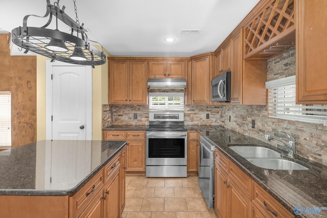 kitchen with sink, dark stone countertops, backsplash, hanging light fixtures, and stainless steel appliances