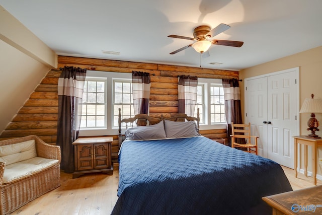 bedroom with ceiling fan, light hardwood / wood-style flooring, a closet, and rustic walls