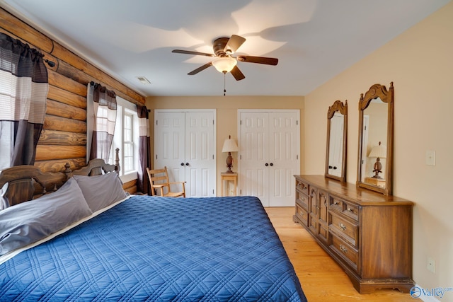 bedroom featuring light wood-type flooring, two closets, rustic walls, and ceiling fan