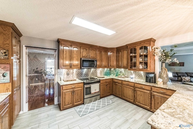 kitchen featuring light hardwood / wood-style flooring, a textured ceiling, appliances with stainless steel finishes, tasteful backsplash, and light stone counters