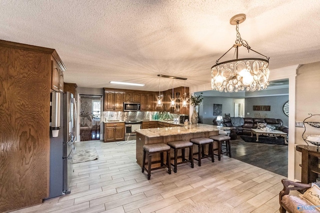 kitchen with light stone counters, light hardwood / wood-style flooring, pendant lighting, a kitchen bar, and appliances with stainless steel finishes