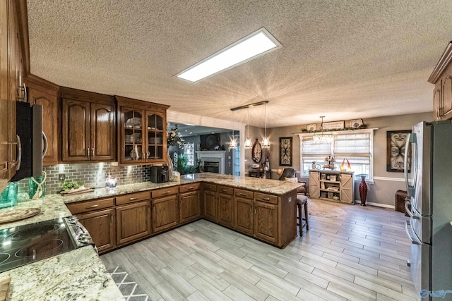 kitchen featuring kitchen peninsula, appliances with stainless steel finishes, a textured ceiling, decorative light fixtures, and light hardwood / wood-style flooring