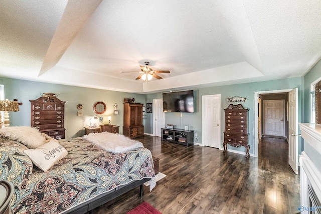 bedroom featuring a textured ceiling, ceiling fan, dark wood-type flooring, and a tray ceiling