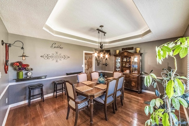 dining space featuring dark hardwood / wood-style floors, a textured ceiling, and a tray ceiling