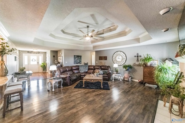 living room with a raised ceiling, ceiling fan, dark hardwood / wood-style flooring, and a textured ceiling