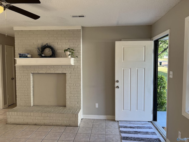 foyer with visible vents, ceiling fan, a textured ceiling, a fireplace, and light tile patterned flooring