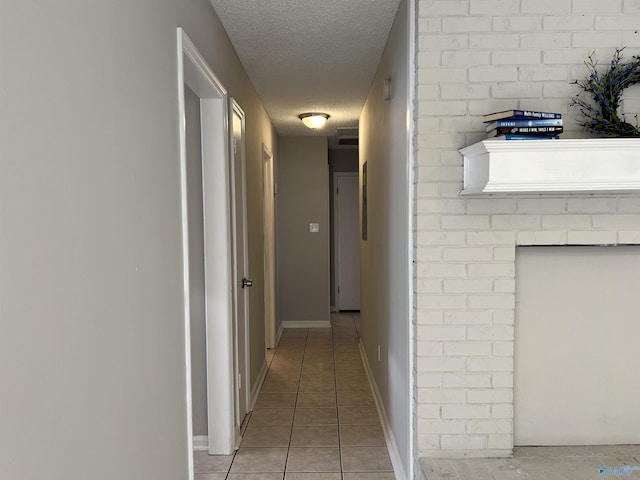 hallway with baseboards, a textured ceiling, and light tile patterned flooring