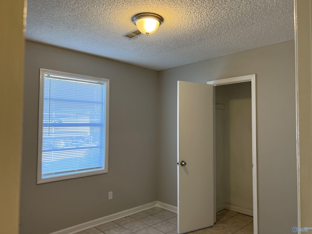 unfurnished bedroom featuring light tile patterned floors, baseboards, visible vents, and a textured ceiling