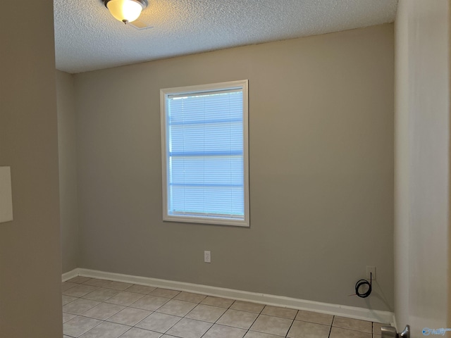 empty room with light tile patterned floors, baseboards, and a textured ceiling