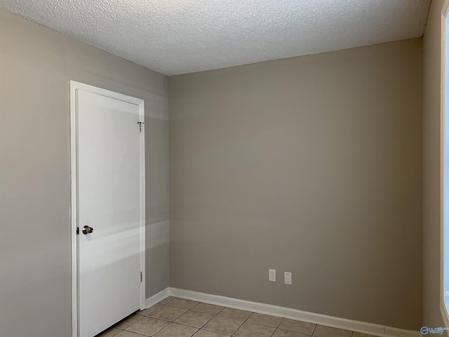 spare room with light tile patterned floors, baseboards, and a textured ceiling