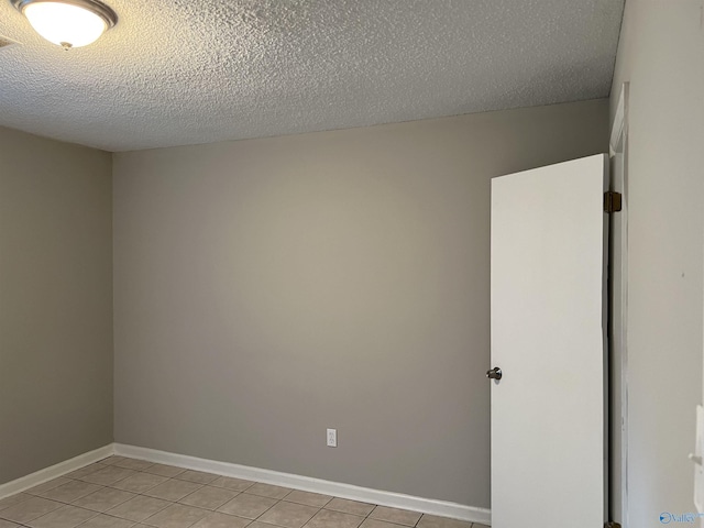 spare room with a textured ceiling, baseboards, and light tile patterned floors