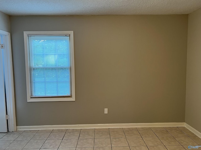 unfurnished room with a textured ceiling, light tile patterned flooring, and baseboards