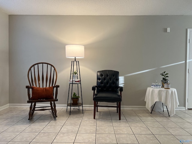 living area with light tile patterned flooring, a textured ceiling, and baseboards