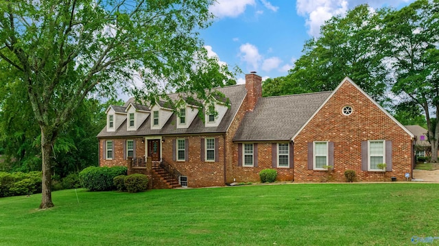 cape cod house with a shingled roof, a chimney, a front lawn, and brick siding