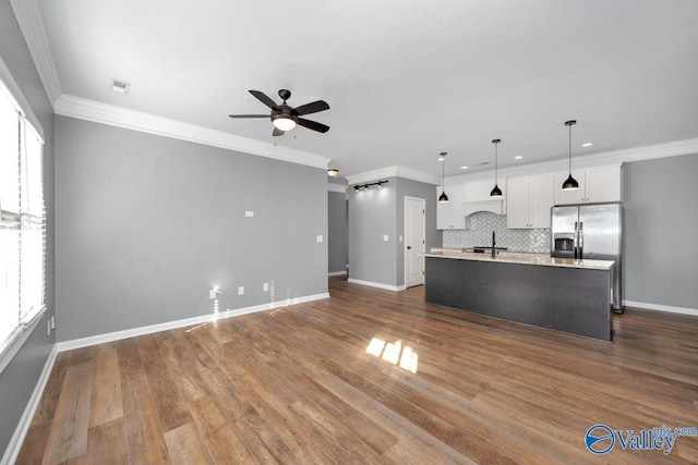 kitchen with backsplash, ornamental molding, decorative light fixtures, a center island with sink, and white cabinetry