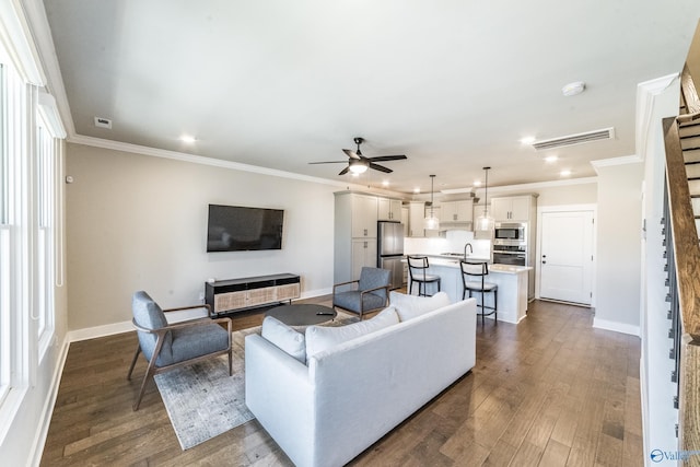 living room featuring ceiling fan, a fireplace, sink, dark wood-type flooring, and ornamental molding