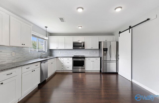 kitchen featuring white cabinets, a barn door, appliances with stainless steel finishes, dark hardwood / wood-style floors, and pendant lighting