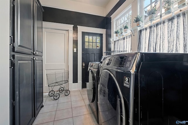 laundry area featuring washing machine and clothes dryer, light tile patterned floors, and cabinets