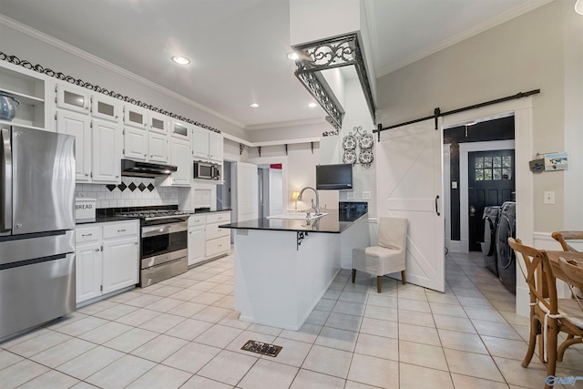 kitchen with kitchen peninsula, appliances with stainless steel finishes, washer and dryer, a barn door, and white cabinets