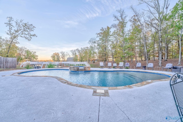 pool at dusk featuring an in ground hot tub and pool water feature