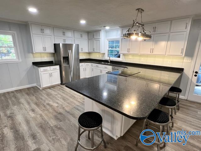 kitchen with a breakfast bar, light hardwood / wood-style flooring, stainless steel refrigerator with ice dispenser, and white cabinets