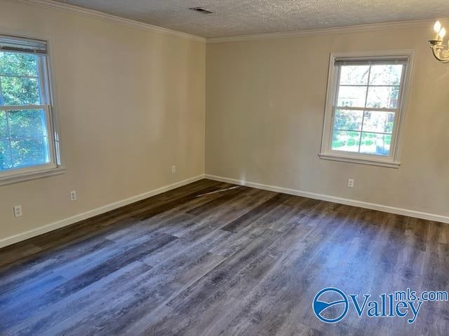 empty room featuring dark wood-type flooring, a textured ceiling, ornamental molding, and a wealth of natural light