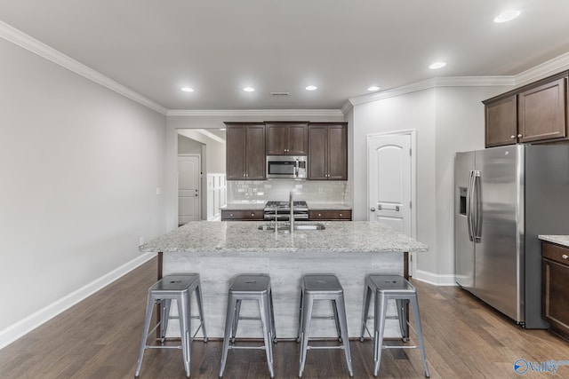 kitchen featuring a kitchen island with sink, sink, decorative backsplash, light stone countertops, and appliances with stainless steel finishes