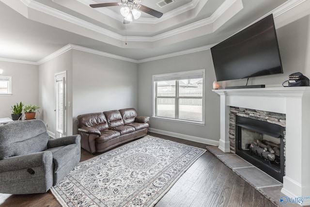 living room featuring dark hardwood / wood-style flooring, a stone fireplace, a raised ceiling, and ornamental molding