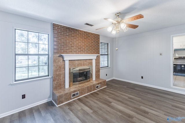 unfurnished living room with a tiled fireplace, dark hardwood / wood-style floors, and a healthy amount of sunlight