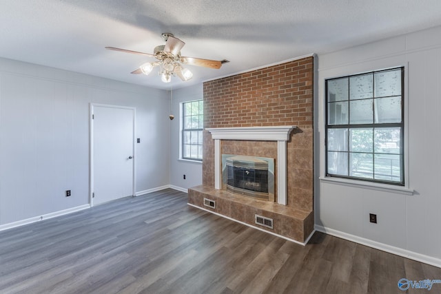 unfurnished living room with a textured ceiling, dark hardwood / wood-style floors, ceiling fan, and a large fireplace