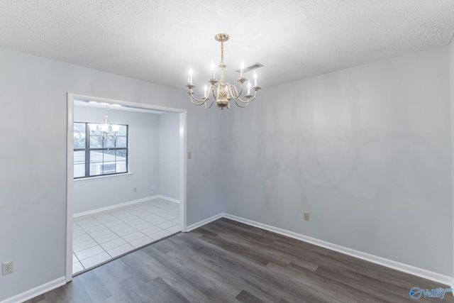 unfurnished room featuring visible vents, a textured ceiling, wood finished floors, and a notable chandelier
