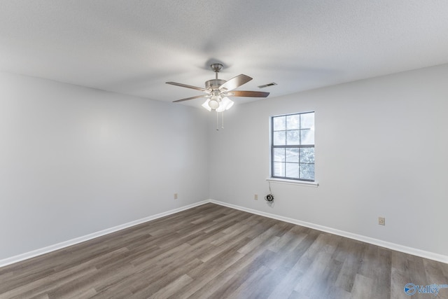 empty room featuring a textured ceiling, visible vents, ceiling fan, baseboards, and dark wood-style flooring