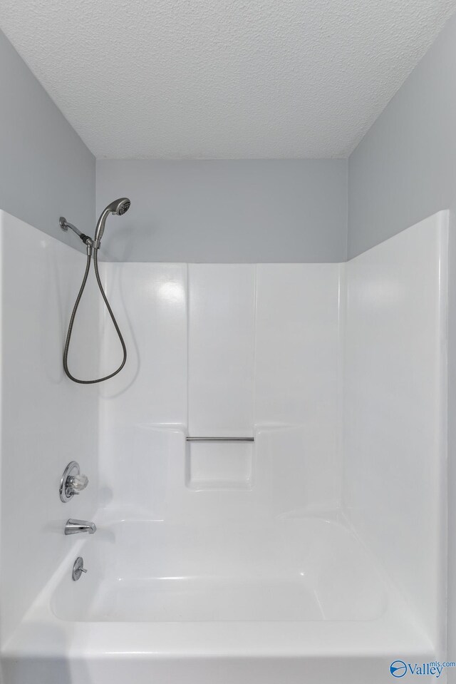 bathroom with a textured ceiling and bathtub / shower combination