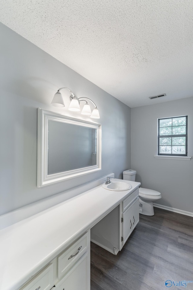 bathroom featuring wood finished floors, toilet, vanity, visible vents, and a textured ceiling