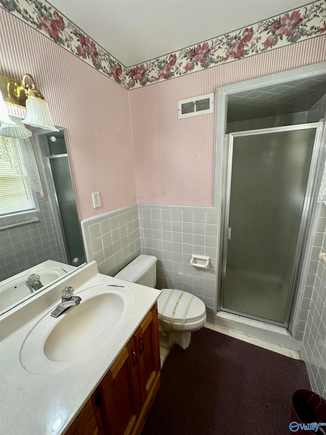 bathroom with tile walls, vanity, toilet, and a shower with shower door