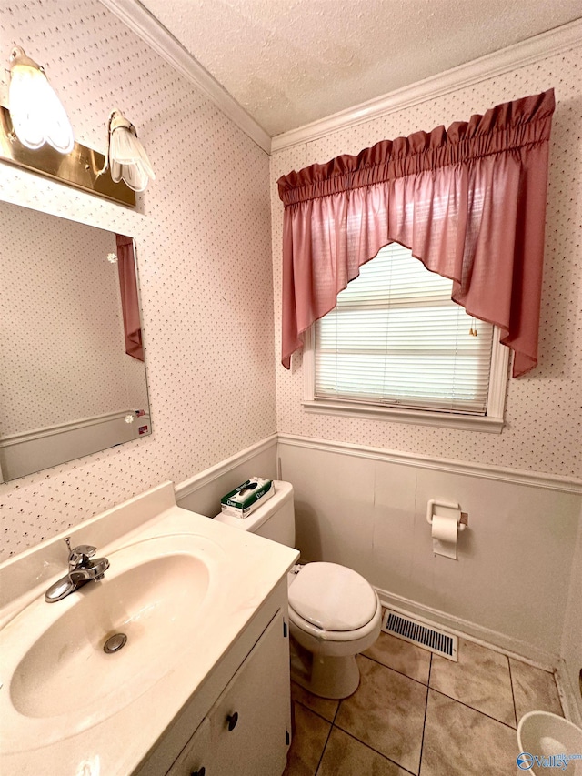 half bath with wainscoting, wallpapered walls, a textured ceiling, and visible vents