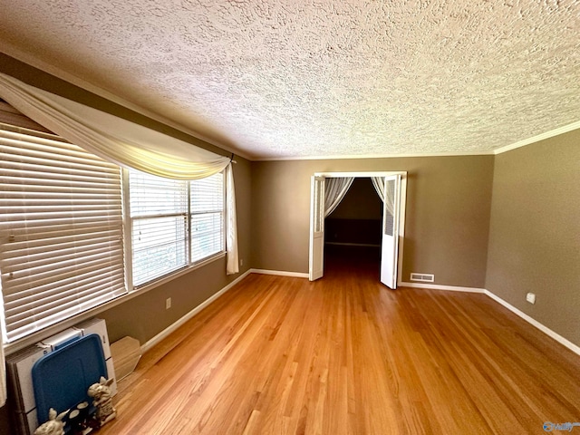 unfurnished room with crown molding, a textured ceiling, and light hardwood / wood-style flooring