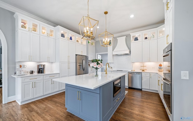 kitchen with custom exhaust hood, stainless steel appliances, light countertops, glass insert cabinets, and white cabinetry