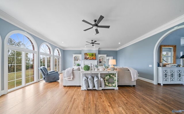 living room with arched walkways, wood finished floors, a ceiling fan, baseboards, and ornamental molding