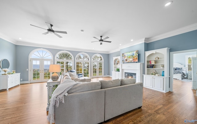 living area featuring crown molding, recessed lighting, a glass covered fireplace, wood finished floors, and baseboards