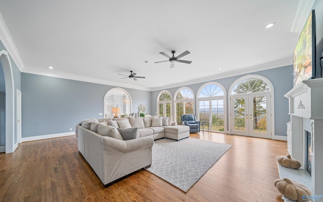 living area featuring a warm lit fireplace, baseboards, arched walkways, and crown molding