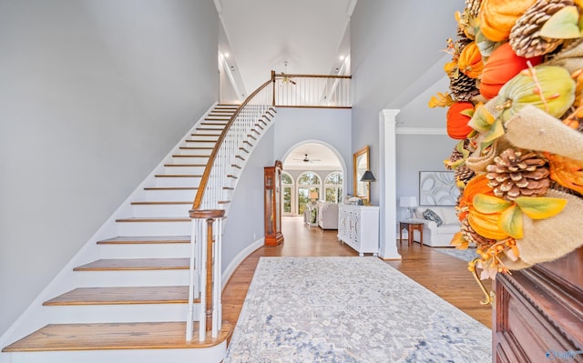 entrance foyer with arched walkways, a high ceiling, wood finished floors, stairway, and decorative columns