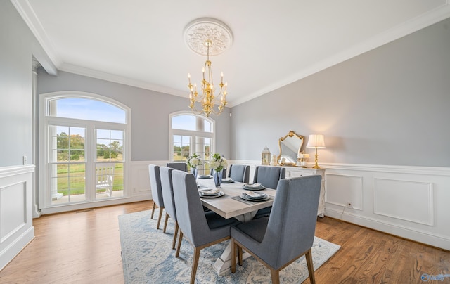 dining space with a decorative wall, light wood-style floors, wainscoting, an inviting chandelier, and crown molding