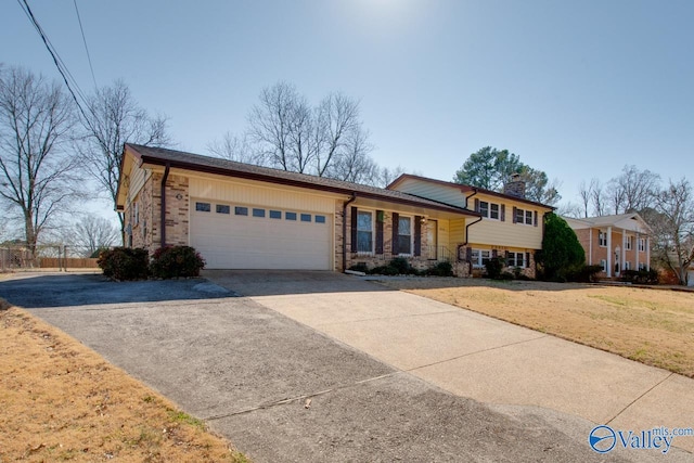 tri-level home featuring brick siding, a chimney, an attached garage, a front yard, and driveway