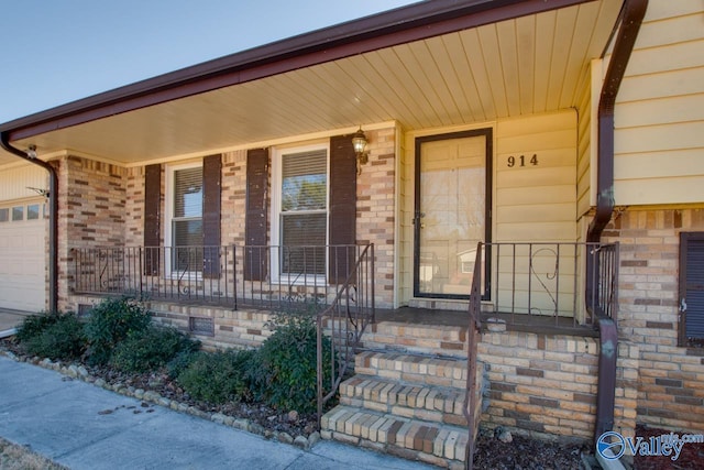 view of exterior entry featuring a porch, brick siding, and a garage