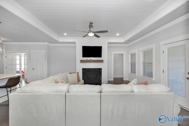 living room featuring a fireplace, ceiling fan, ornamental molding, a tray ceiling, and dark wood-type flooring