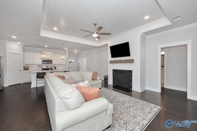 living room featuring a fireplace, a raised ceiling, ceiling fan, ornamental molding, and dark hardwood / wood-style floors