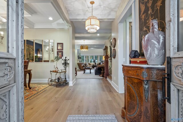 entrance foyer with ornamental molding, beam ceiling, light wood-type flooring, and a chandelier