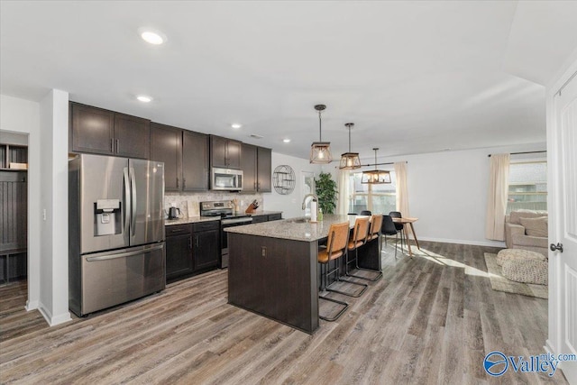 kitchen featuring appliances with stainless steel finishes, a kitchen island with sink, a kitchen breakfast bar, pendant lighting, and dark brown cabinetry